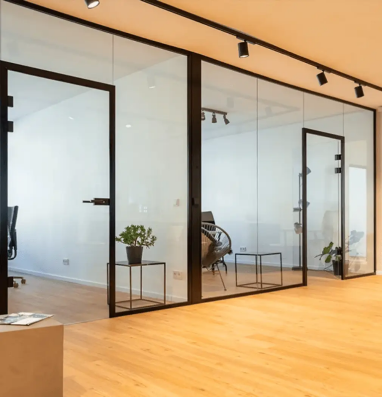 Das moderne Bürointerieur besticht durch verglaste Räume mit eleganten schwarzen Rahmen, Holzböden und Deckenstrahlern. Eine kleine Pflanze in einem schwarzen Topf steht in der Ecke neben einem leeren Stuhl und schafft eine digitale Krankenhausatmosphäre der Ruhe und Konzentration.