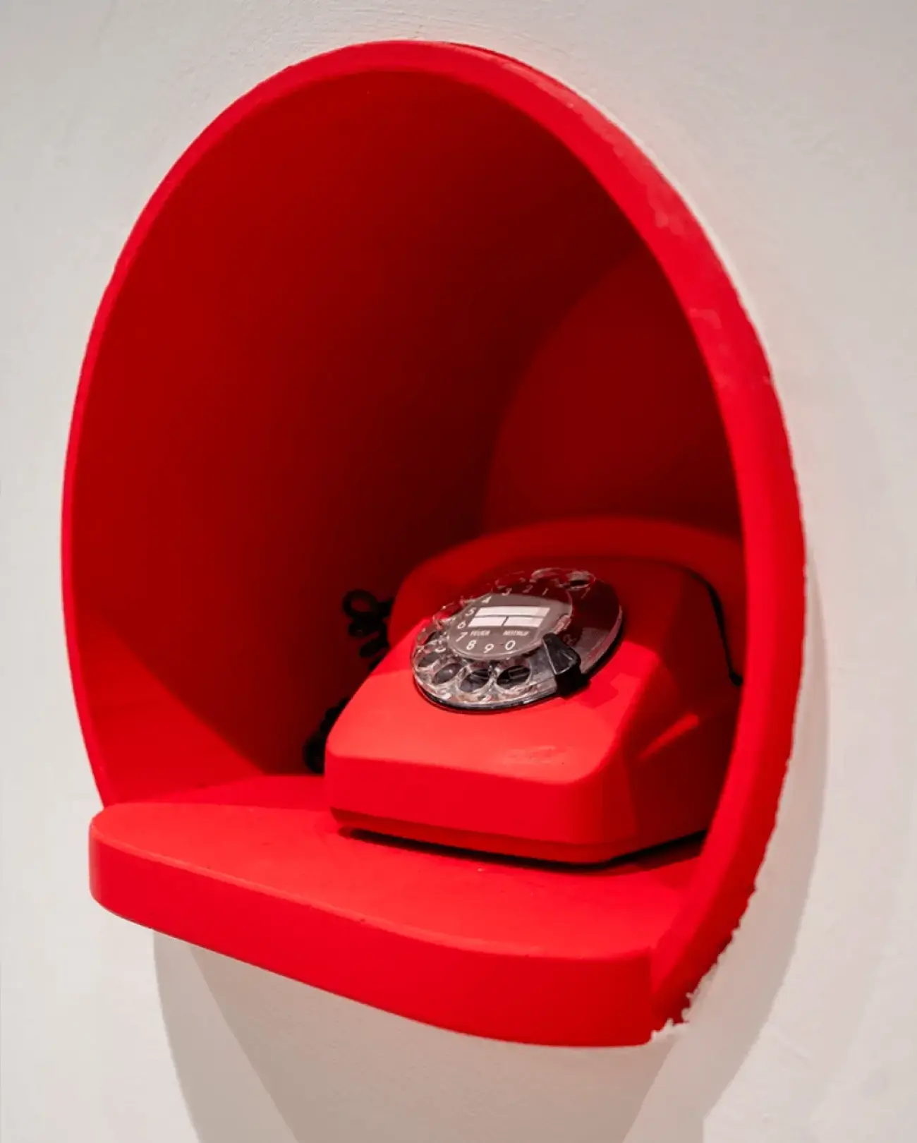 Ein rotes Wählscheibentelefon steht in einer passend roten Wandnische mit geschwungener Oberkante vor weißem Hintergrund – ein markantes Statement, das an die kühnen Designentscheidungen von DigitalSpital Business Innovator erinnert.